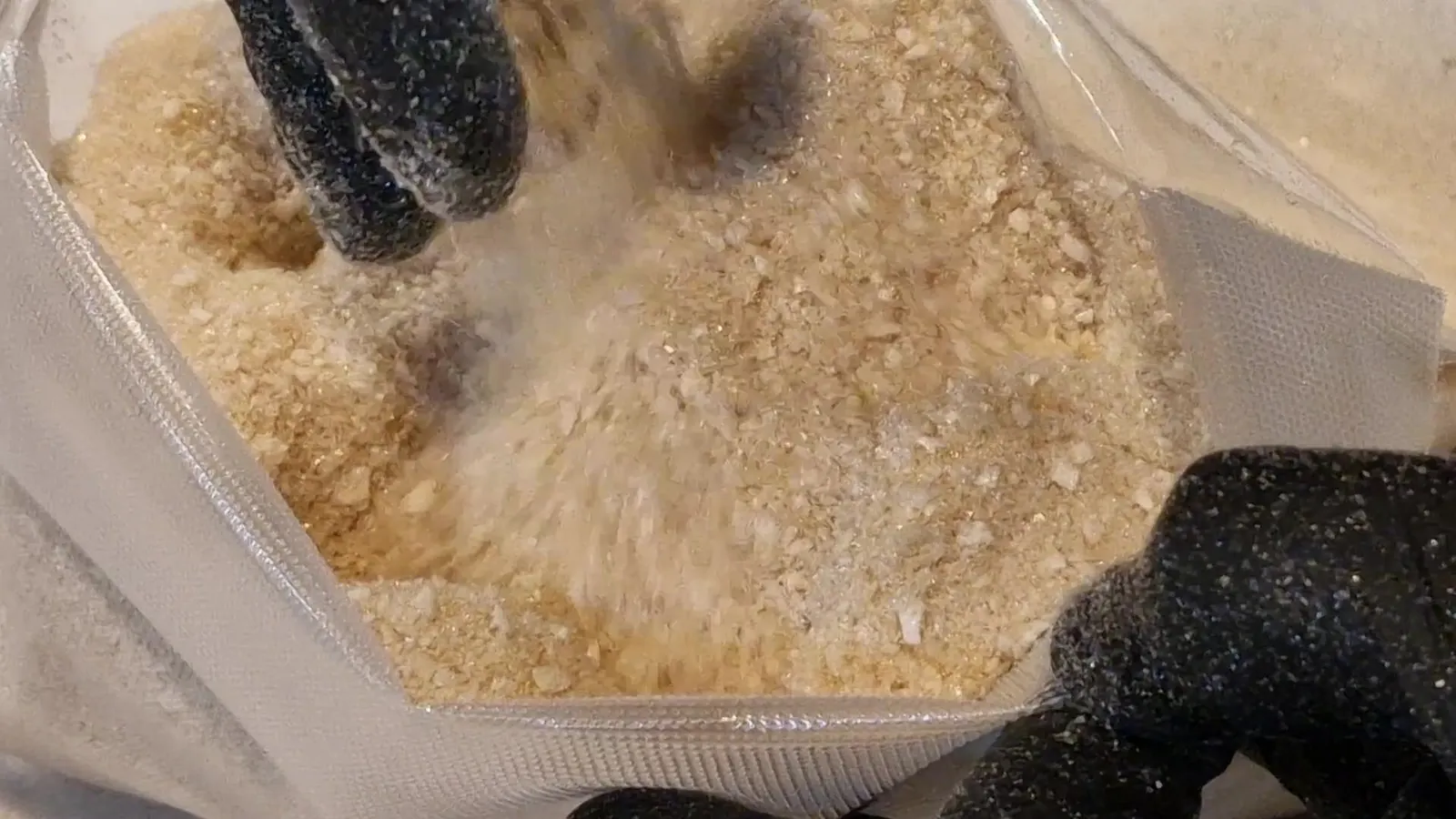 Manos enguantadas vertiendo caldo de vacuno liofilizado, grueso y de color dorado pálido, en una bolsa barrera transparente